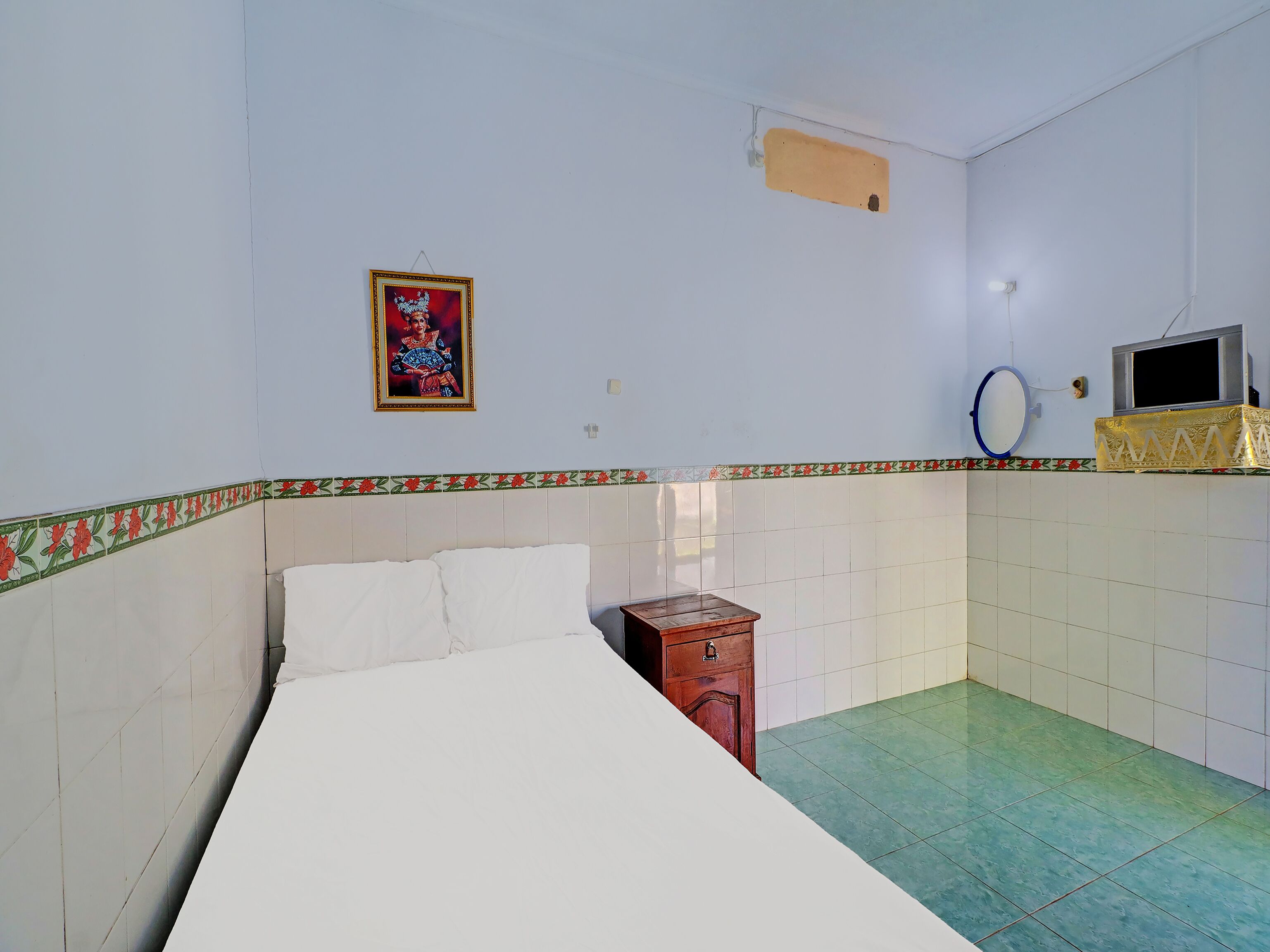 A room with a bed, a small wooden nightstand, a wall-mounted TV, and a decorative border along the lower wall.