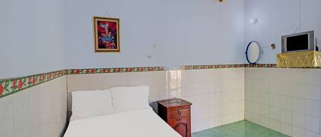 A room with a bed, a small wooden nightstand, a wall-mounted TV, and a decorative border along the lower wall.