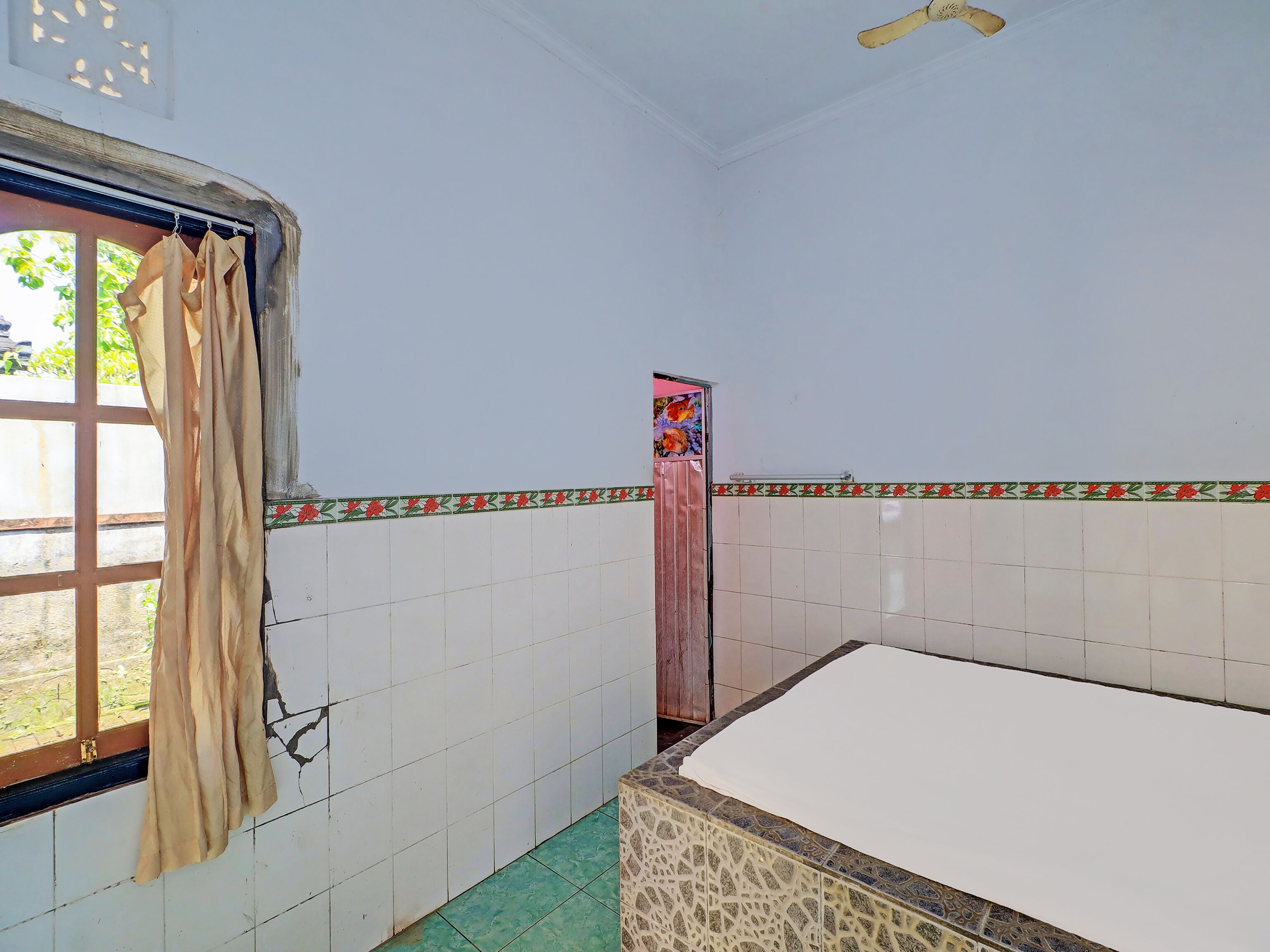 A room with a bed, a window with curtains, tiled walls, and a door.