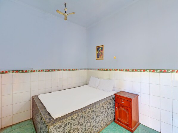 Un dormitorio con cama, un aparador de madera, un ventilador de techo y un detalle decorativo en la pared.