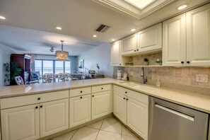 A kitchen with white cabinets, a stainless steel dishwasher, and a large island with a sink.