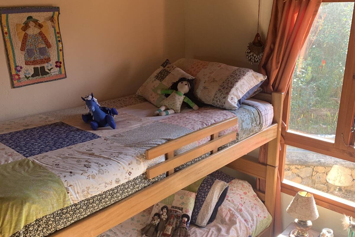 A bunk bed room with a window, a small table with a lamp, and decorative pillows.
