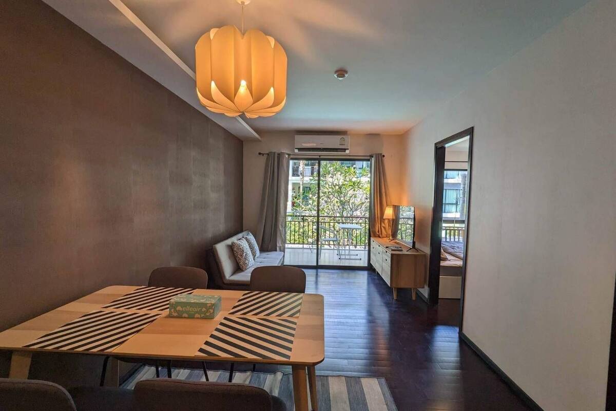 A modern hotel room with a dining area, a sofa, a balcony with a view, and a large window.