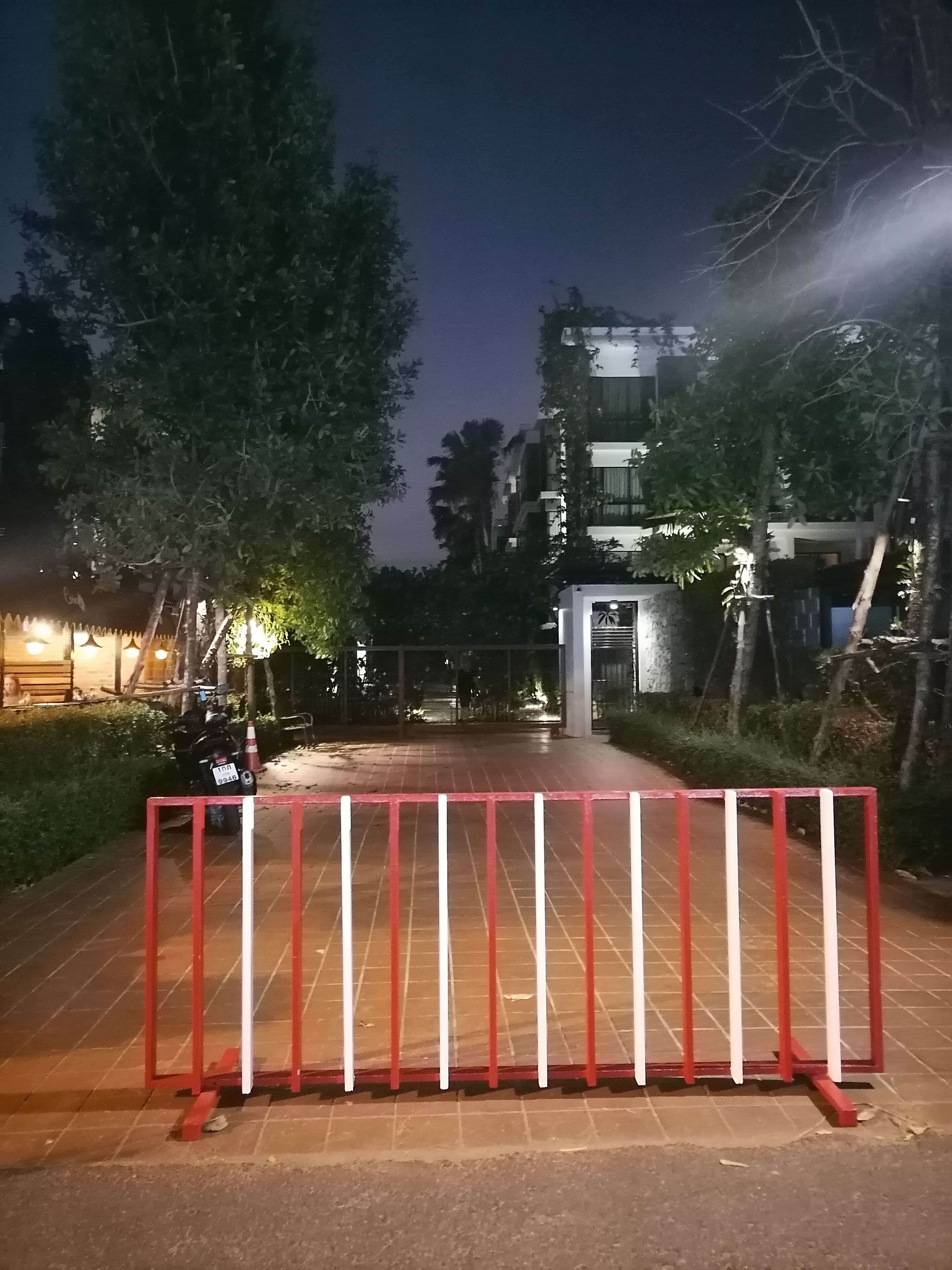 A gated entrance with a red and white barrier, a paved pathway, and a building in the background.