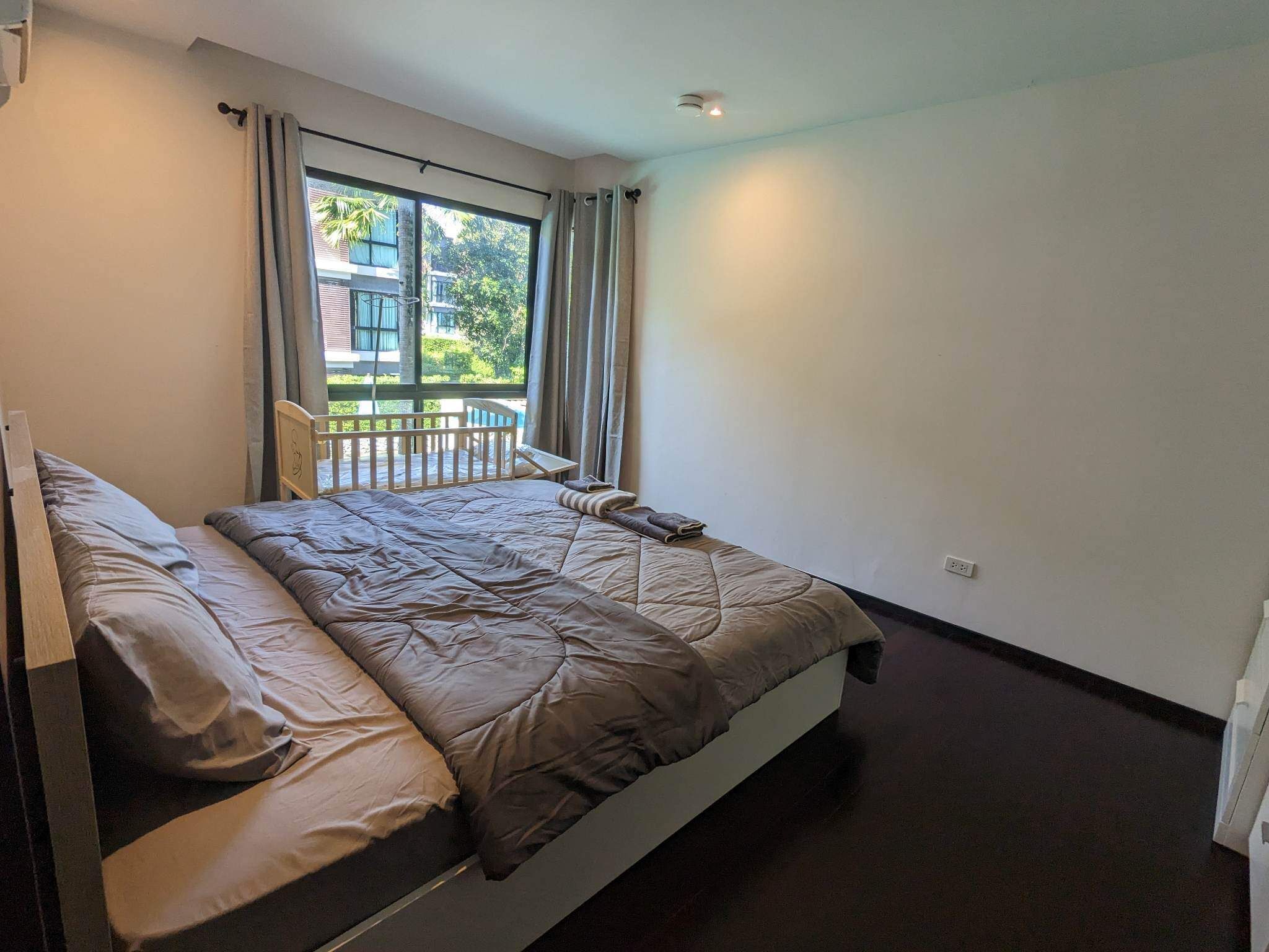 Ein Schlafzimmer mit Bett, einem Fenster mit Vorhängen und Blick auf einen Balkon und Gebäude im Freien.