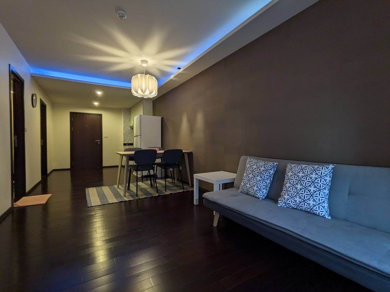 Ein modernes Wohnzimmer mit einer Couch, gemusterten Kissen, einem Essbereich mit Stühlen und einer Küche im Hintergrund.