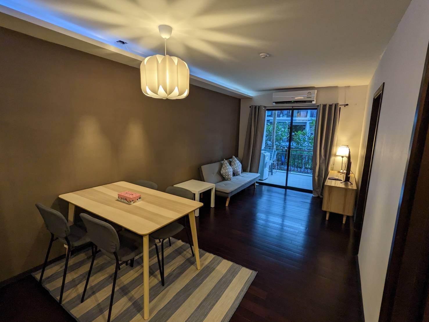 Ein modernes Wohnzimmer mit Essbereich, einer Couch, einer Lampe und Blick ins Freie.