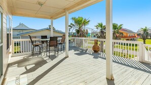 A covered outdoor area with a wooden deck, a table with chairs, and a large vase. - Banana Cabana – Gulf Views & Good Vibes (Surfside Beach)