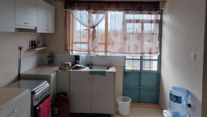 Uma cozinha compacta com armários brancos, fogão a gás, pia e janela com cortinas leves.