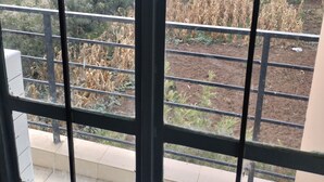 Vista de varanda com grades de metal, com vista para um campo de plantações e edifícios ao longe.