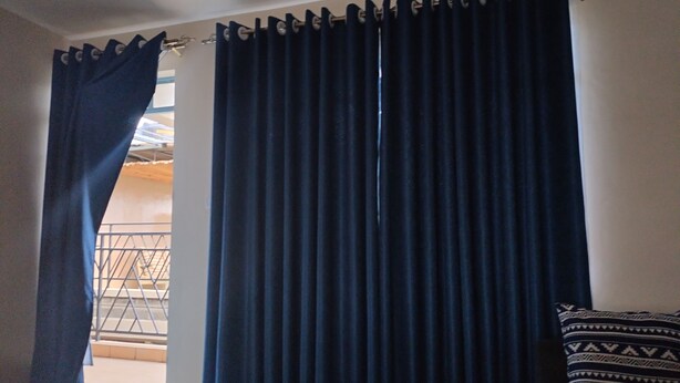 Quarto com uma grande janela coberta por cortinas azul-escuras, almofada estampada em um sofá branco e corrimão de metal do lado de fora da janela.