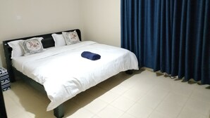 Cama bem arrumada com lençóis brancos e uma toalha azul dobrada, cabeceira preta e dois travesseiros decorativos.