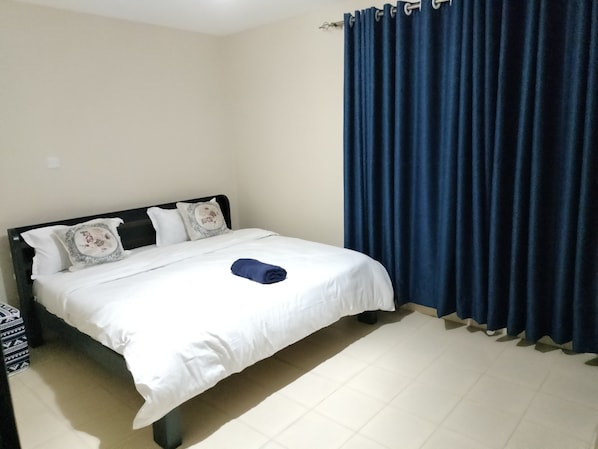 A neatly made bed with white linens and a folded blue towel, a black headboard, and two decorative pillows. - Executive 1&2 Broom Airbnb in Gilgil Nakuru (Gilgil)