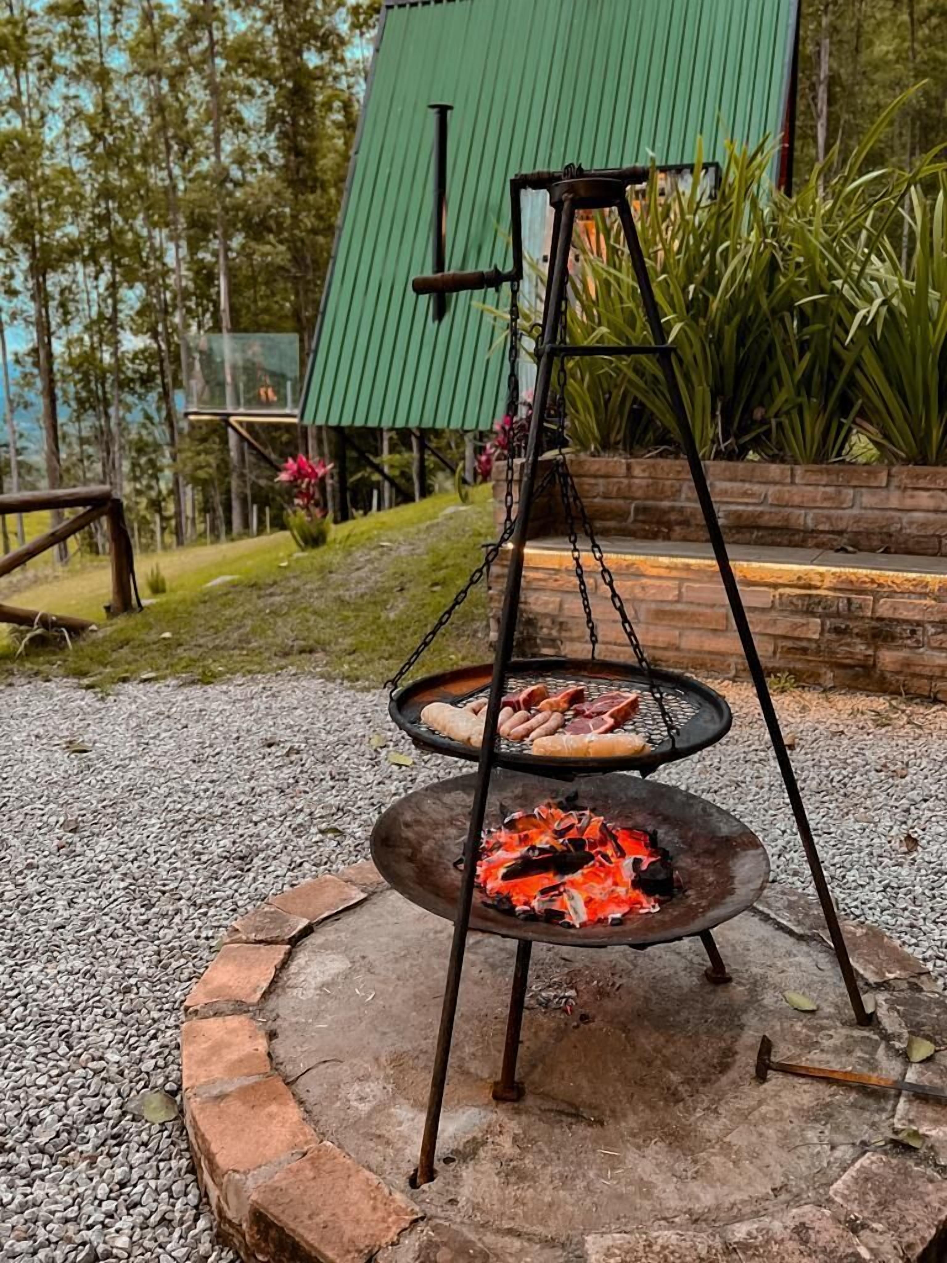 En grill med tre våningar för utomhusbruk, där köttet tillagas på den nedre våningen. Grillen står på en sockel av sten och är omgiven av grus.