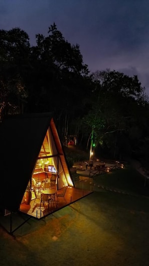 A cozy, triangular-shaped outdoor structure with a glass facade, a dining area, and a small kitchen visible inside.