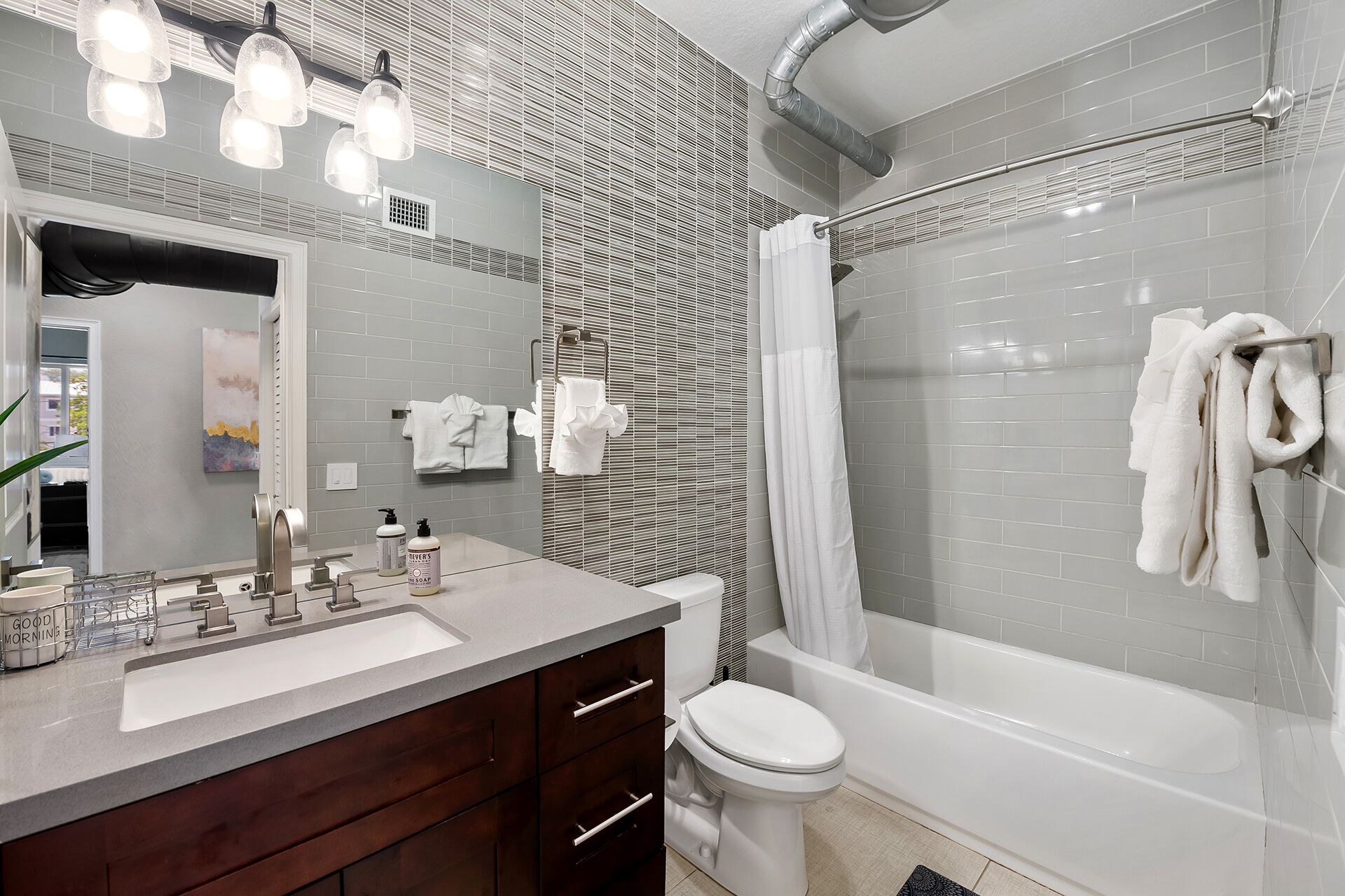 A modern bathroom with a large mirror, a vanity with a sink, a toilet, and a bathtub with a shower curtain.