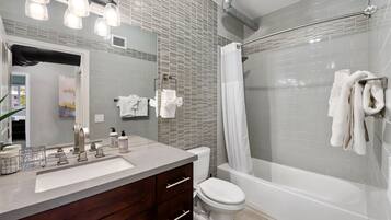 A modern bathroom with a large mirror, a vanity with a sink, a toilet, and a bathtub with a shower curtain.