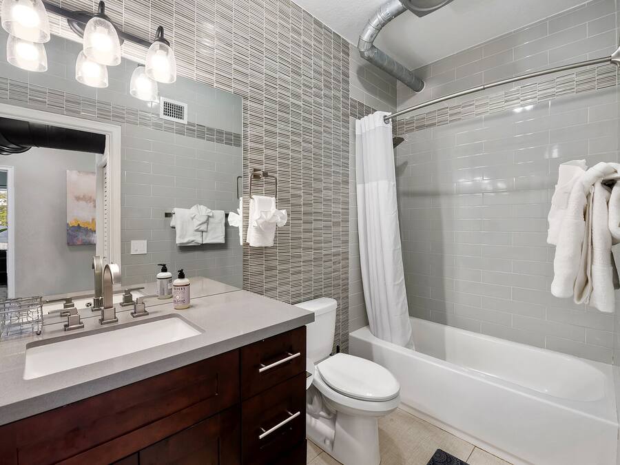A modern bathroom with a large mirror, a vanity with a sink, a toilet, and a bathtub with a shower curtain.
