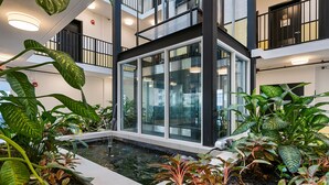 Un moderno atrio interior con cerramiento de vidrio, una fuente de agua y abundante vegetación.