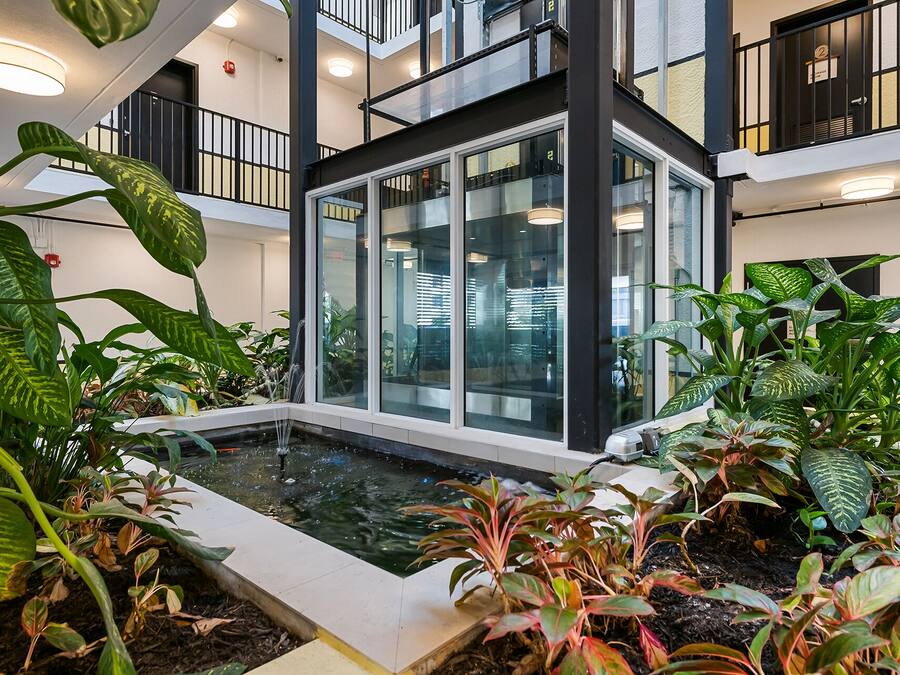 Un moderno atrio interior con cerramiento de vidrio, una fuente de agua y abundante vegetación.
