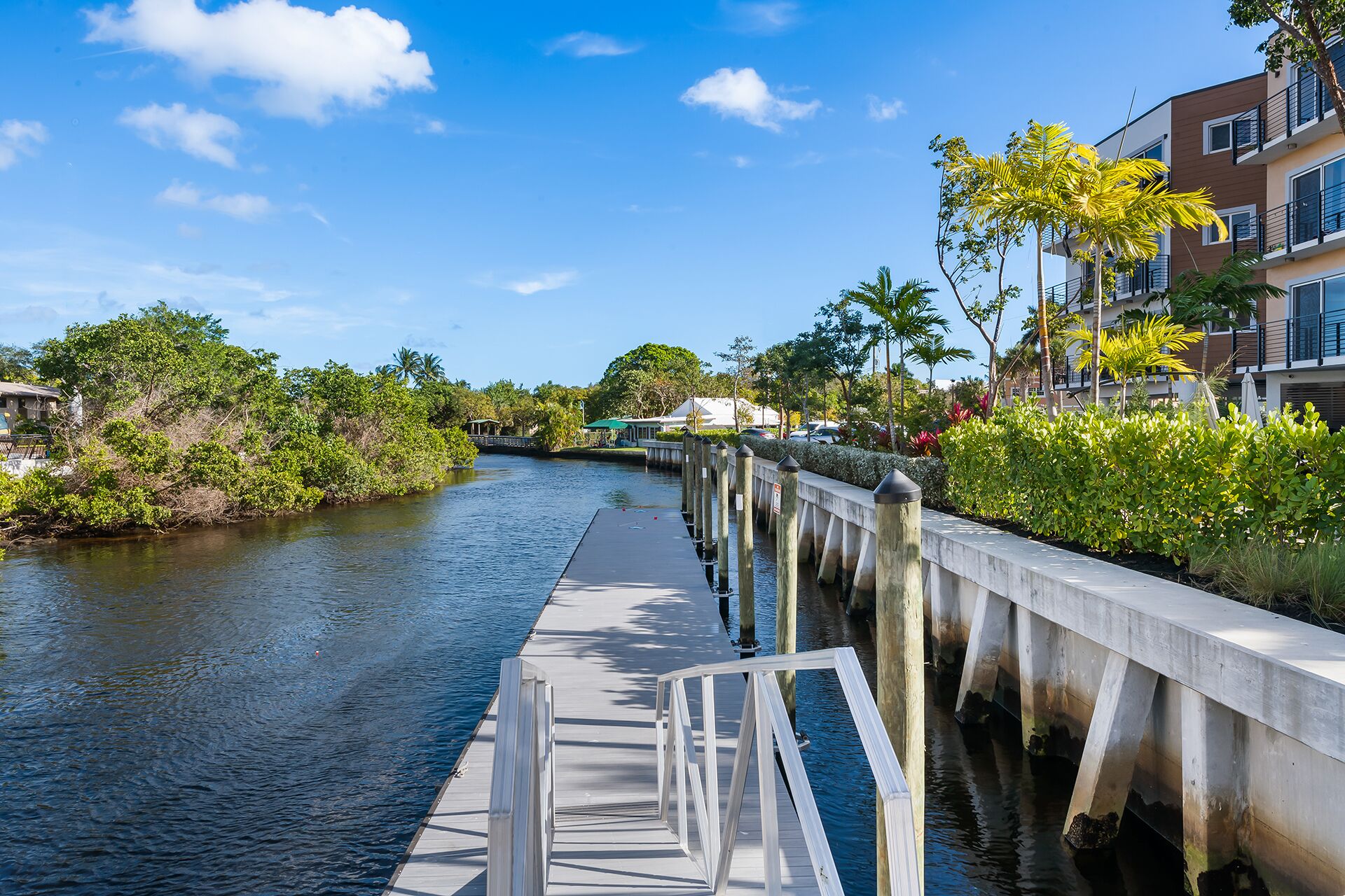 A waterfront walkway with a concrete barrier, a calm river, and lush greenery.