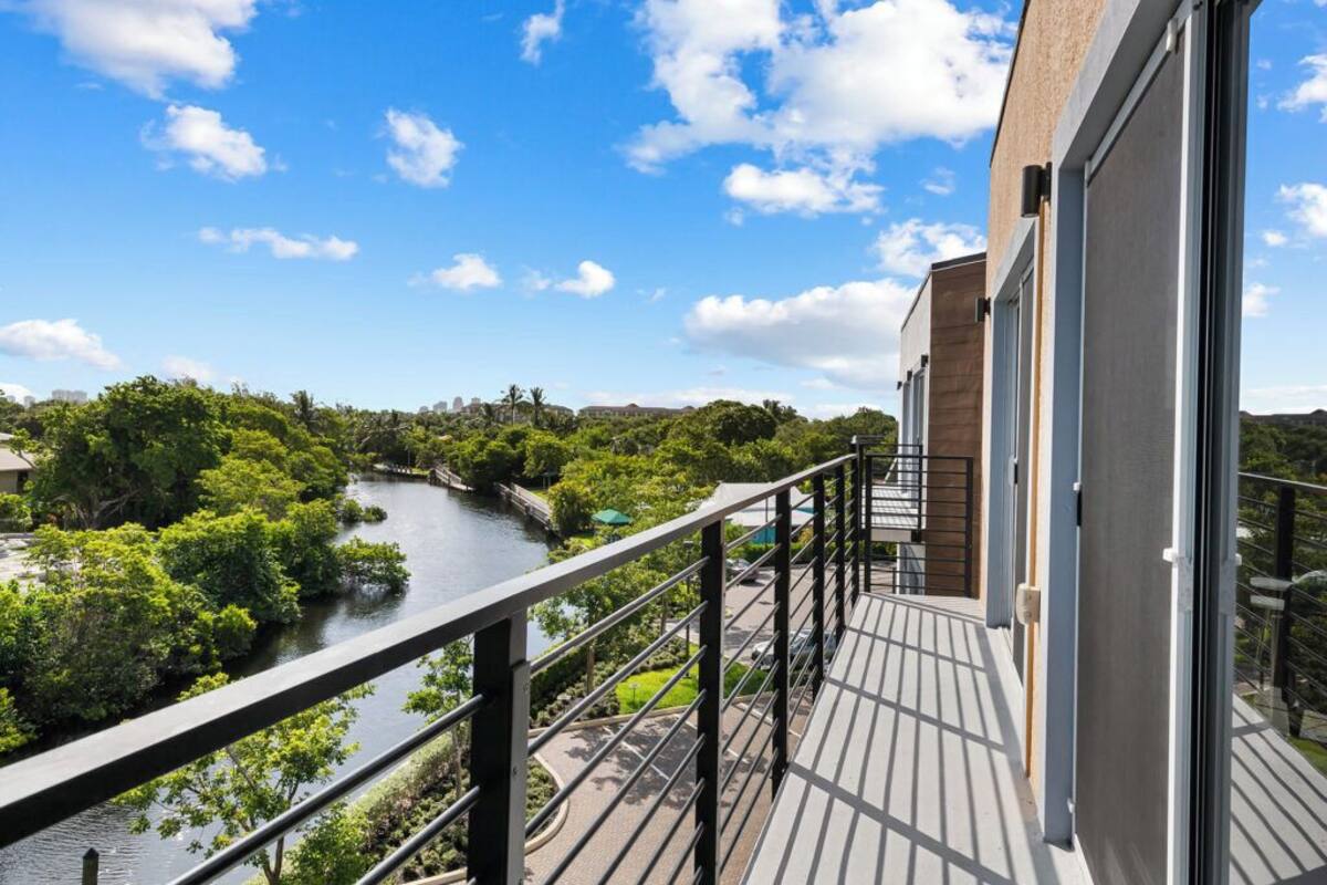 A balcony with a view of a river and greenery, a modern building facade, and a clear sky.