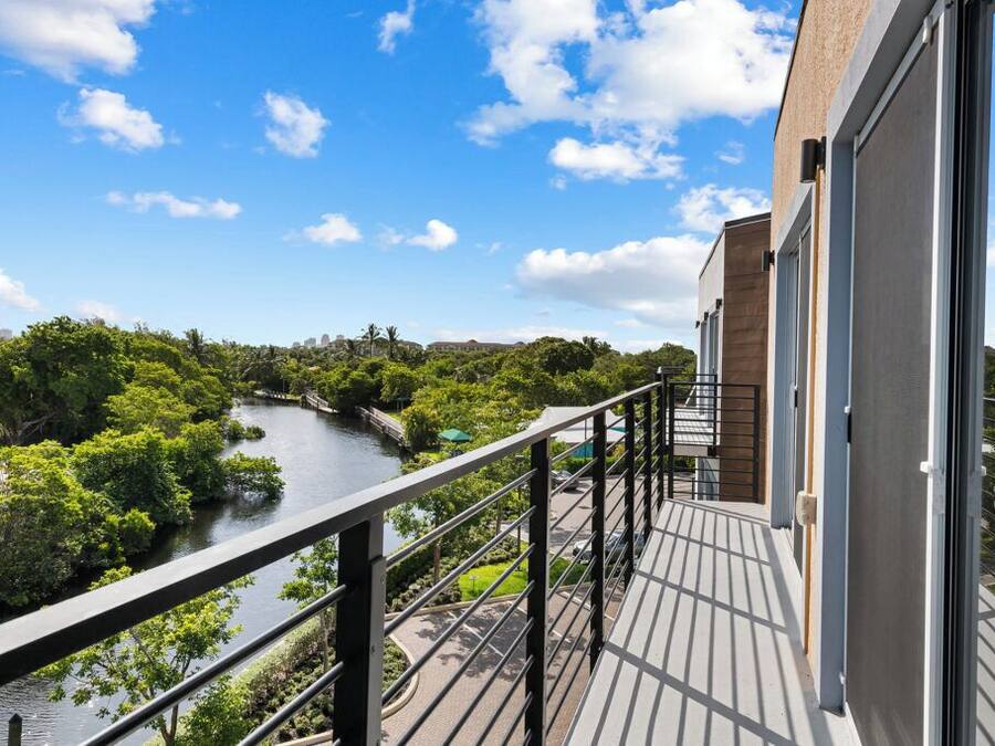 Un balcon donnant sur une rivière et sur un paysage verdoyant, la façade d’un immeuble moderne et un ciel dégagé.