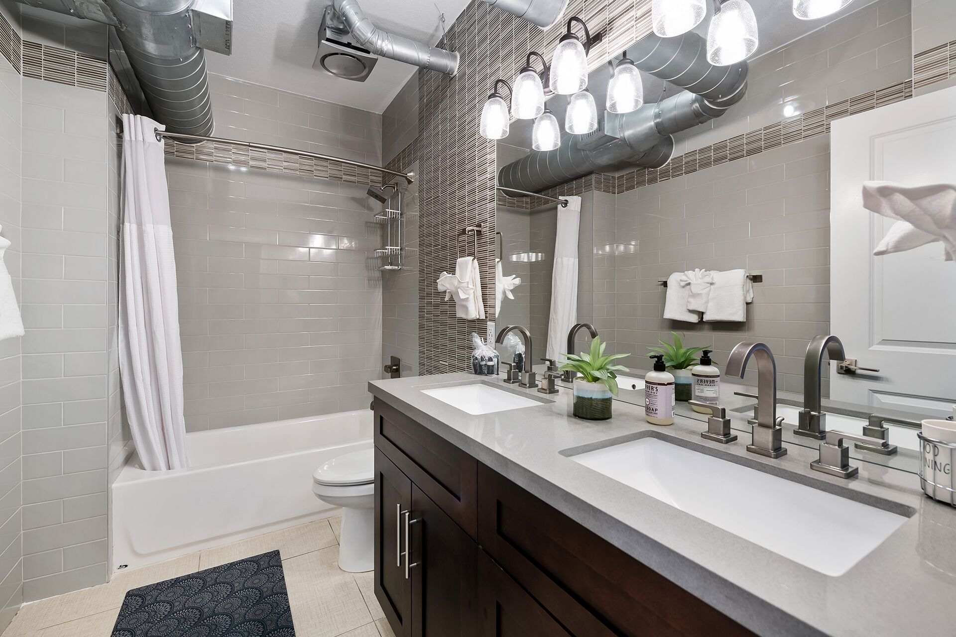 Une salle de bain moderne avec deux lavabos, une baignoire et des toilettes. On y trouve plusieurs porte-serviettes et un grand miroir au-dessus des lavabos.