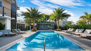 Una piscina con sillones de descanso, palmeras y un edificio moderno con balcones.