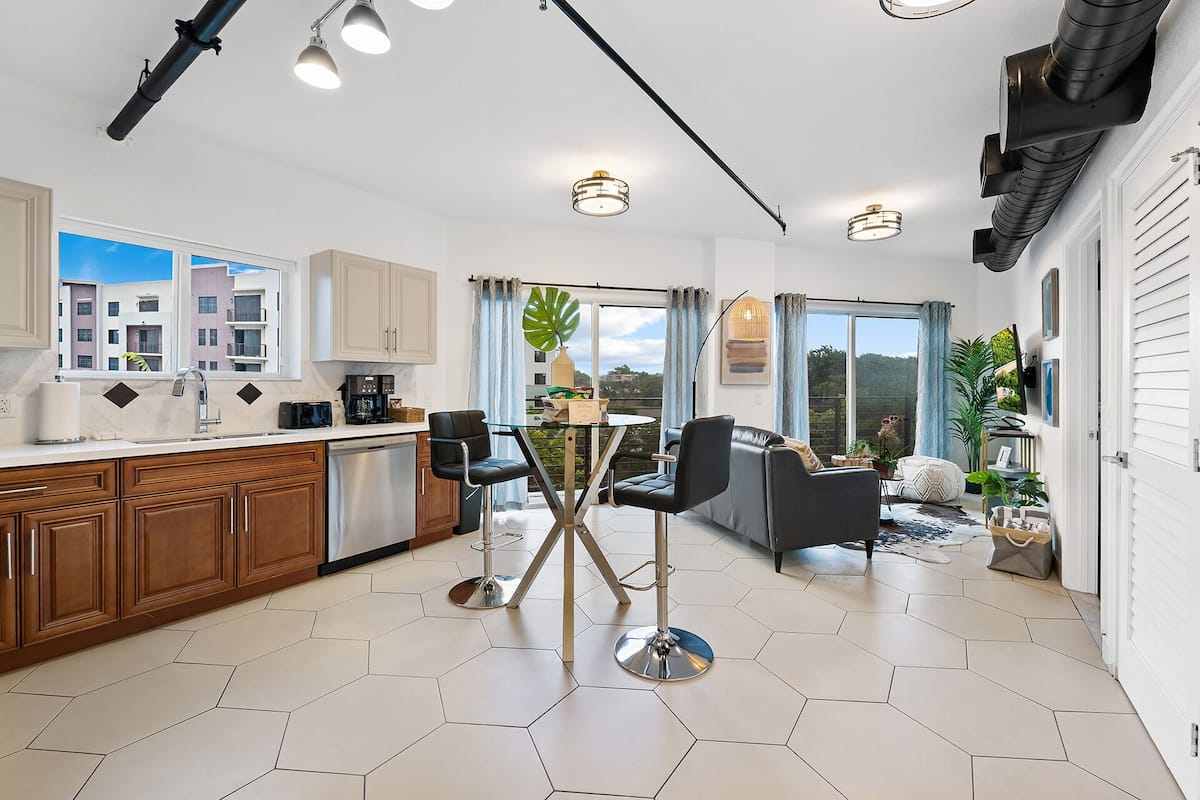 A modern kitchen with a dining area, large windows, and a view of buildings.