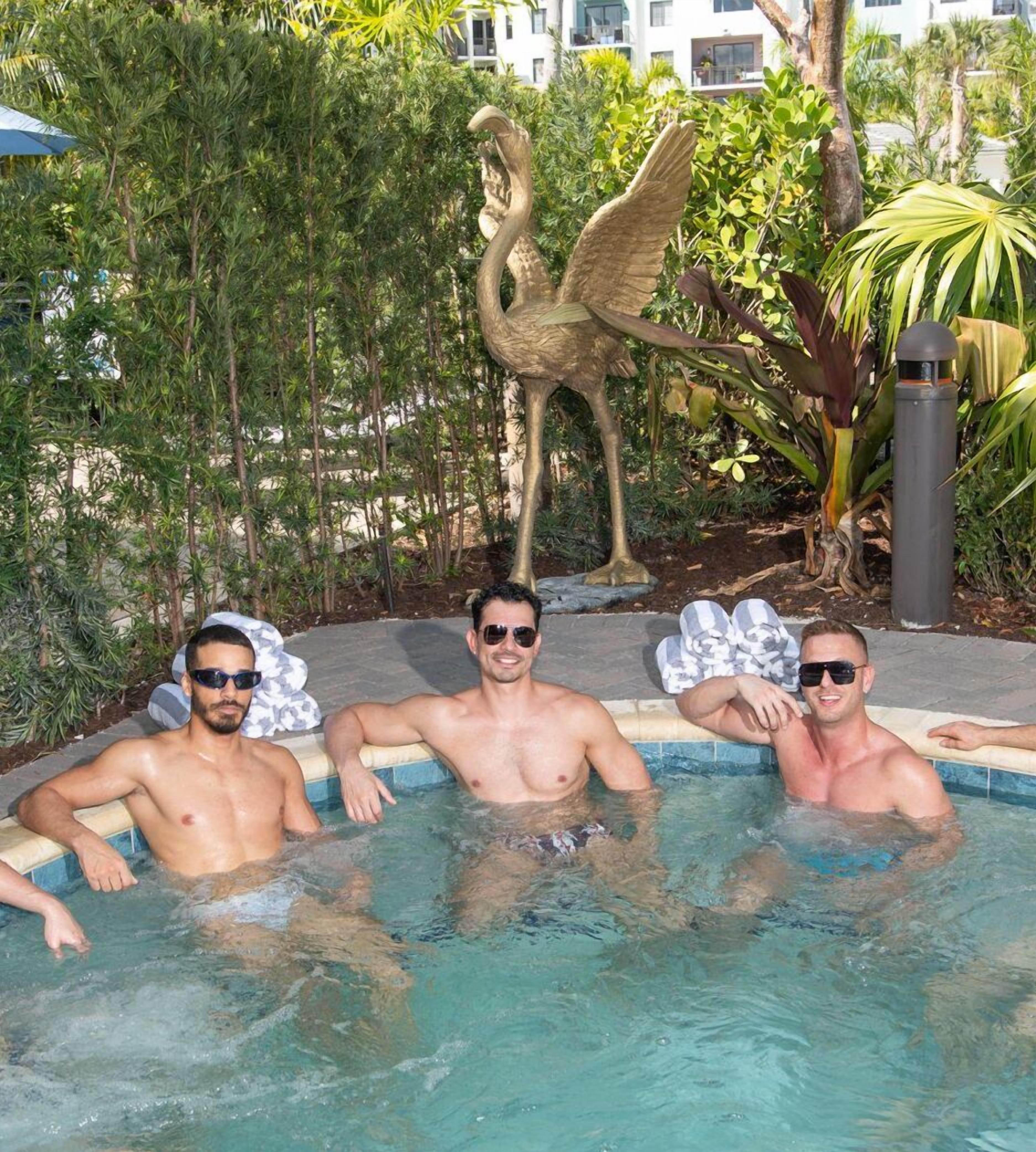 Three men in a swimming pool with a statue of a bird in the background.