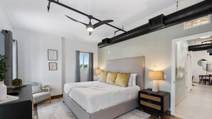 Un dormitorio moderno con una cama grande, mesitas de noche, ventilador de techo y vistas al exterior.