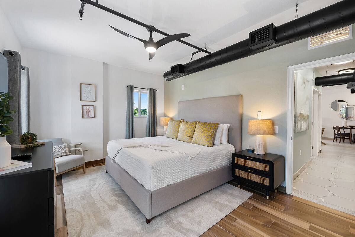 A modern bedroom with a large bed, bedside tables, a ceiling fan, and a view of the outside.