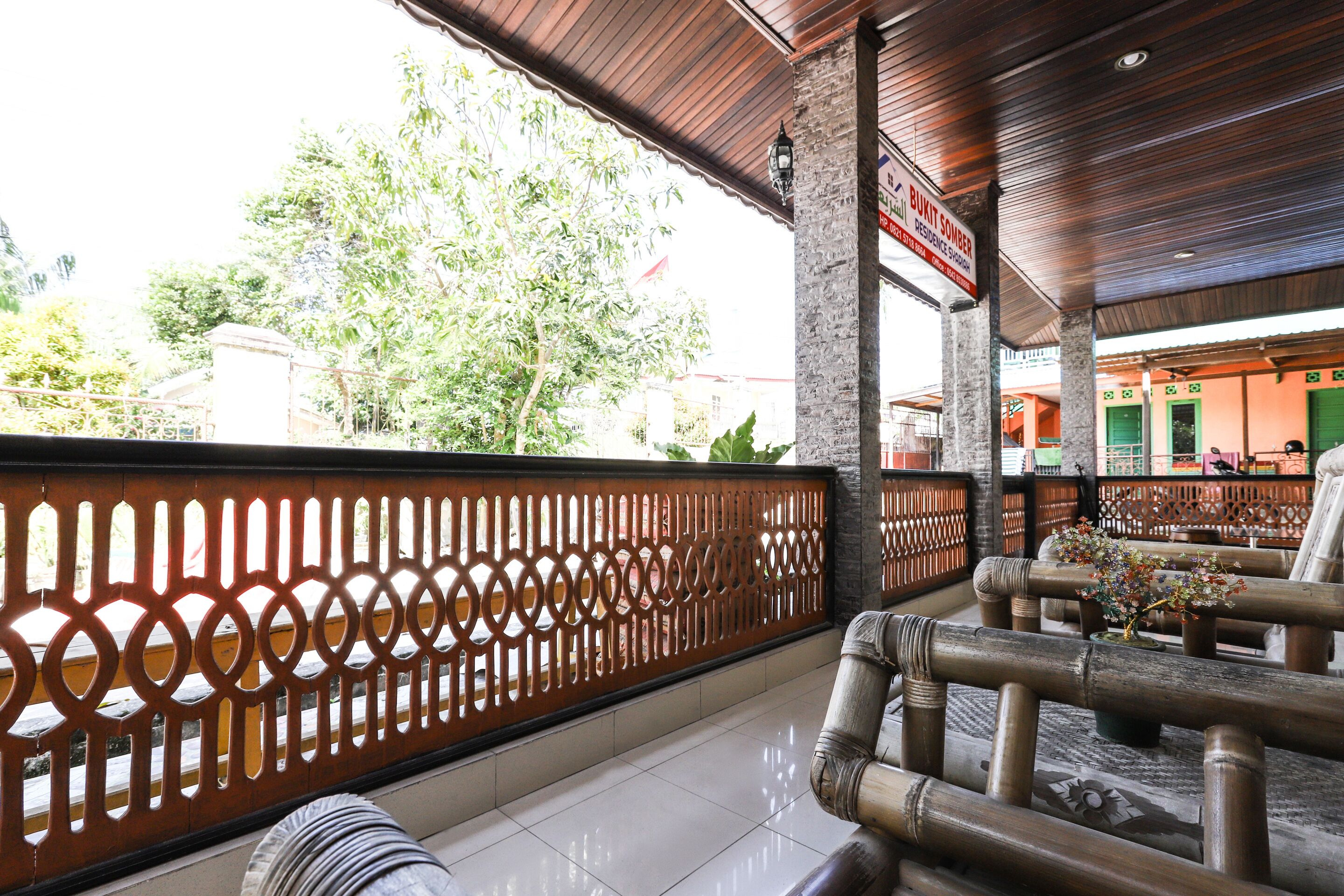 A covered outdoor seating area with a wooden fence, a sign for a residence, and a view of trees and buildings in the background.