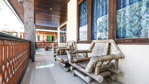 A corridor with traditional bamboo furniture, a tiled floor, and a view of a building with green doors. - Hotel O Bukit Somber Residence Syariah (Balikpapan)