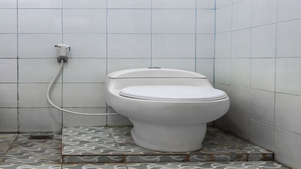 A small, tiled bathroom with a toilet and a visible pipe. - Hotel O Bukit Somber Residence Syariah (Balikpapan)