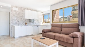 Un apartamento moderno con cocina, sala de estar con sofá y un amplio ventanal con vista a la ciudad.