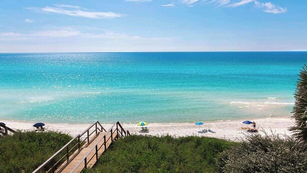 A beach with a wooden walkway leading to the shore, clear blue water, and people relaxing under umbrellas. - Spacious Seagrove Escape Cart Bikes Pool Near Beach (Santa Rosa Beach)