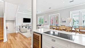 A modern kitchen with white cabinetry and a black countertop, a dining area with wooden chairs, and a living room with a sofa and a TV. - Spacious Seagrove Escape Cart Bikes Pool Near Beach (Santa Rosa Beach)