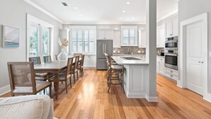 A modern kitchen with white cabinetry, a central island, and a dining area with wooden chairs and a table. - Spacious Seagrove Escape Cart Bikes Pool Near Beach (Santa Rosa Beach)