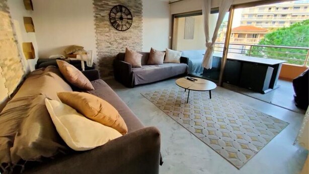 Ein Wohnzimmer mit einer Couch, einem kleinen runden Tisch und einem Balkon mit Blick auf Gebäude.