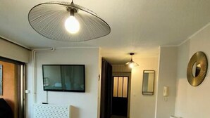 Ein Wohnzimmer mit Sofa, Fernseher, Teppich mit Muster und einer Deckenleuchte.