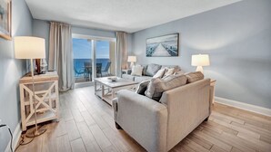 Una sala de estar moderna con sofá, una mesita de centro y una mesa de comedor. Se ve el mar a través de las puertas del balcón.