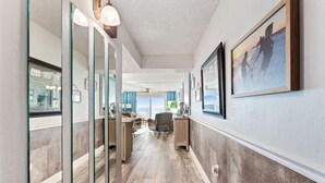 A hallway with a view to the outside, a desk with a chair, and a framed picture on the wall.
