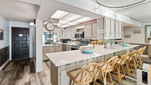 A modern kitchen with a large island, bar stools, and a clock on the wall.