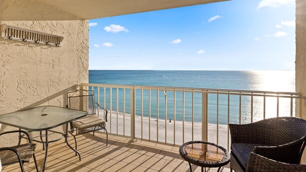 A balcony with a glass table, two wicker chairs, and a small round table.