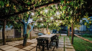 En udendørs terrasse med et bord og stole, omkranset af en pergola med lyskæder.