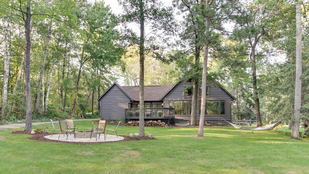A cabin with a deck, surrounded by a grassy yard and tall trees.