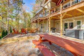 Una terraza de madera con mesas de picnic, un jacuzzi y un espacio cubierto con sillas y una mesa.