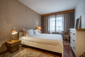A bedroom with a large bed, two bedside lamps, a dresser, and a chair.